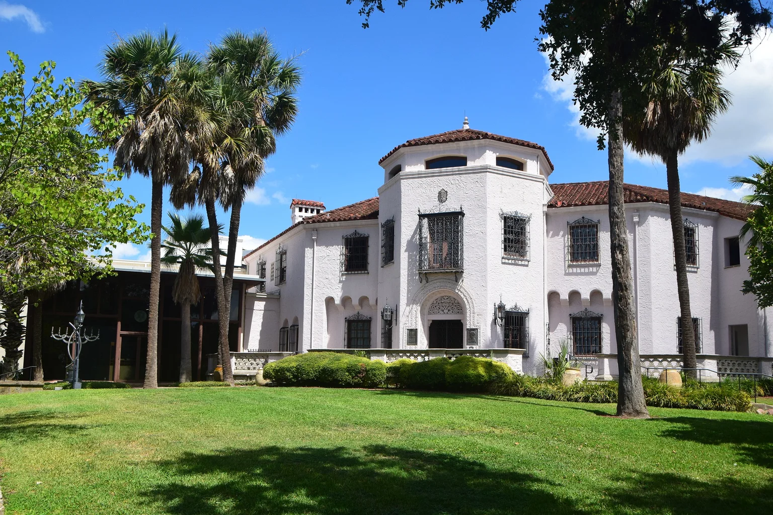 White stucco building with a red tile roof, lawn, and palm trees in Alamo Heights