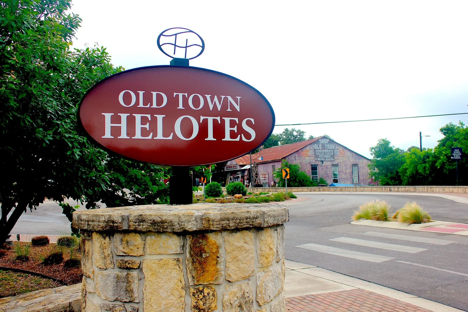 Old Town Helotes sign beside a stone wall and tree-lined street