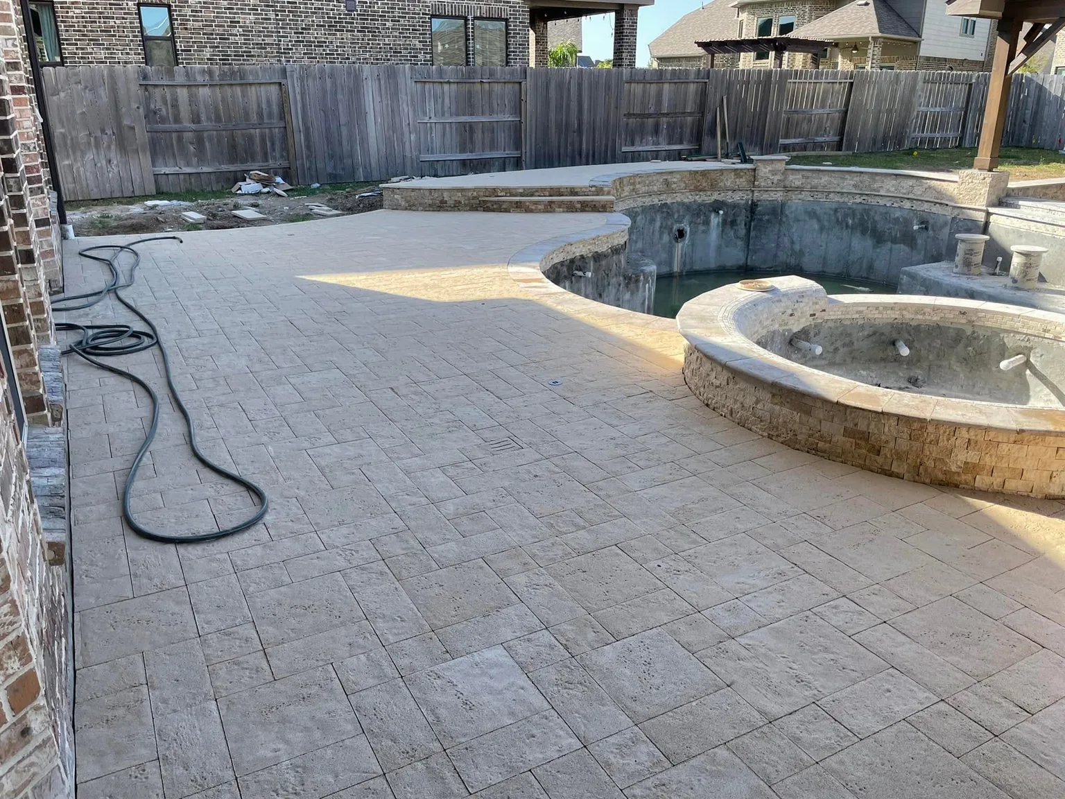 Light stone pool deck and raised spa beside a brick home during renovation